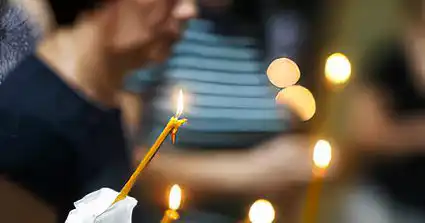 Femei indoliate cu lumanari aprinse la slujba de pomenire a mortilor.